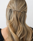 France Luxe long, grey barrette for women pictured holding wavy, blonde hair in a half up hairstyle.