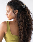 France Luxe small, ivory tortoiseshell claw hair clip for women pictured holding curly, brown hair in a half up hairstyle.