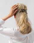 France Luxe large, brown barrette for women pictured holding straight, blonde hair in a half up hairstyle.