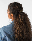 France Luxe large, metallic brown, barrette for women pictured holding curly, brown hair in a half up hairstyle.
