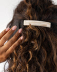 France Luxe medium French barrette for women pictured holding curly, brown hair in a half up hairstyle.
