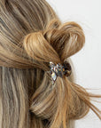 France Luxe mini French claw hair clip for women pictured holding straight, blonde hair in a half up twist hairstyle.