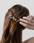 France Luxe medium French barrette for women pictured holding straight, brown hair in a half up hairstyle.