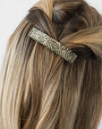 France Luxe medium French barrette for women pictured holding straight, blonde hair in a half up hairstyle.