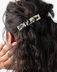 France Luxe medium French barrette for women pictured holding curly, brown hair in a half up hairstyle.