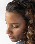 France Luxe thin headband in a metallic burnt sienna and deep chestnut color, pictured holding curly, brown hair in a loose hairstyle.