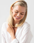 France Luxe thin headband in a rich amber and mahogany brown color, pictured holding straight, blonde hair in a loose hairstyle.