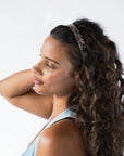 France Luxe wide headband in a marbled gray and charcoal color, pictured holding curly, brown hair in a loose hairstyle.