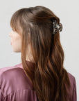France Luxe small French claw hair clip for women pictured holding straight, brown hair in a casual half up hairstyle.