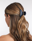 France Luxe small French claw hair clip for women pictured holding wavy, brown hair in a half up hairstyle.