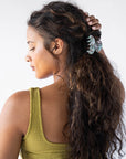 France Luxe small, light blue claw hair clip for women pictured holding curly, brown hair in a half up hairstyle.