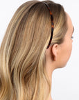 France Luxe thin headband in a Tortoise Shell color, pictured holding straight, blonde hair in a loose hairstyle.