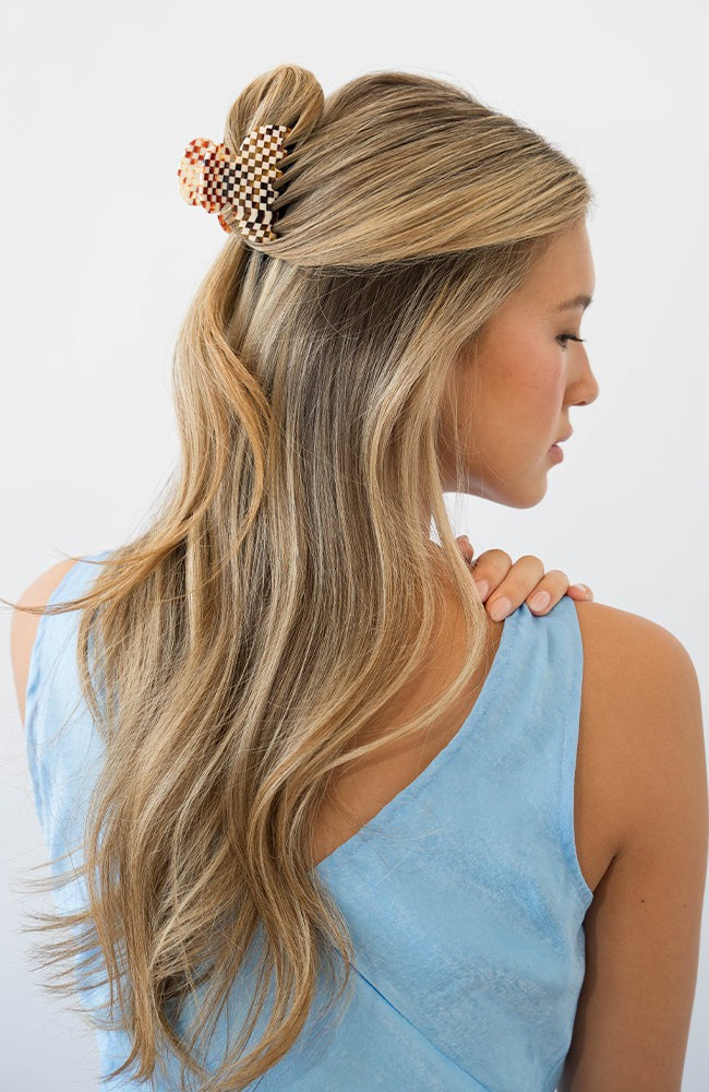 France Luxe small, checkered tortoise claw hair clip for women pictured holding wavy, blonde hair in a half up hairstyle.
