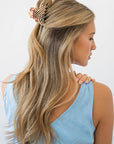 France Luxe small, checkered tortoise claw hair clip for women pictured holding wavy, blonde hair in a half up hairstyle.