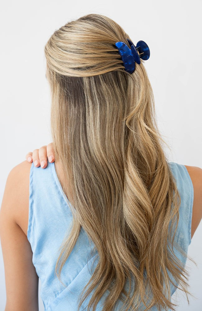 France Luxe small, navy blue claw hair clip for women pictured holding straight, blonde hair in a half up hairstyle.