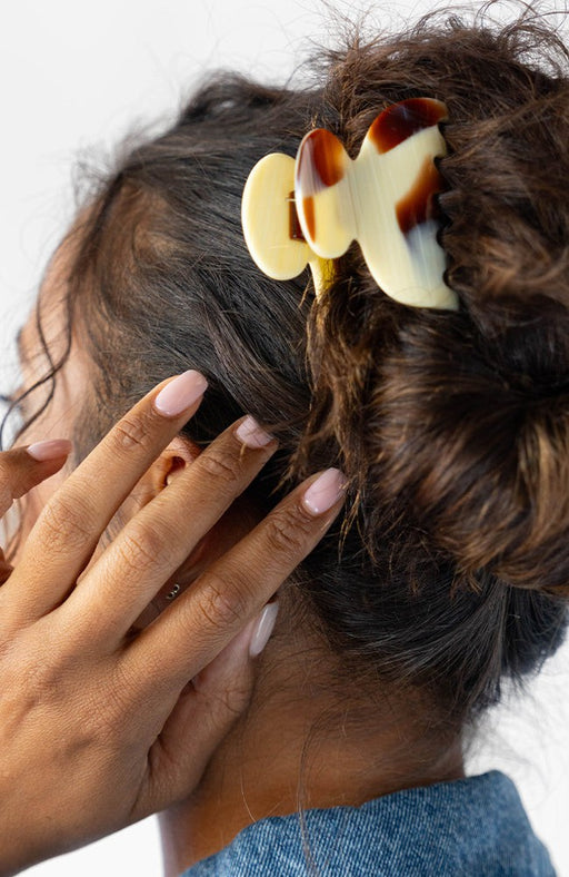 Woman with curly, brown hair styled in a bun with a France Luxe small claw hair clip, horn inspired blend of creamy ivory, warm caramel, and chestnut brown.