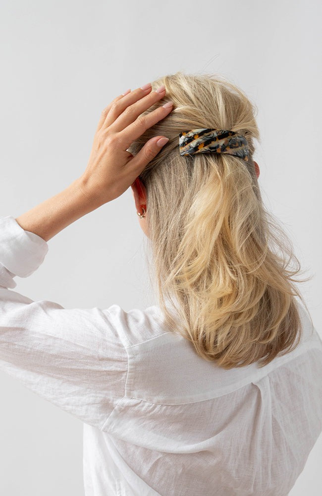 France Luxe large, brown barrette for women pictured holding straight, blonde hair in a half up hairstyle.