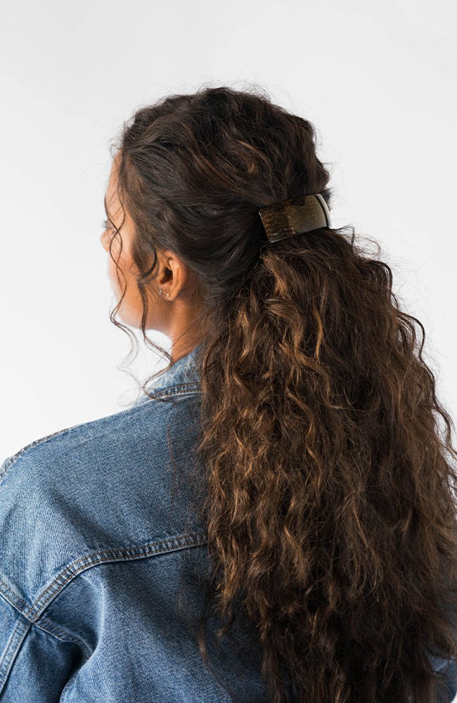 France Luxe large, metallic brown, barrette for women pictured holding curly, brown hair in a half up hairstyle.