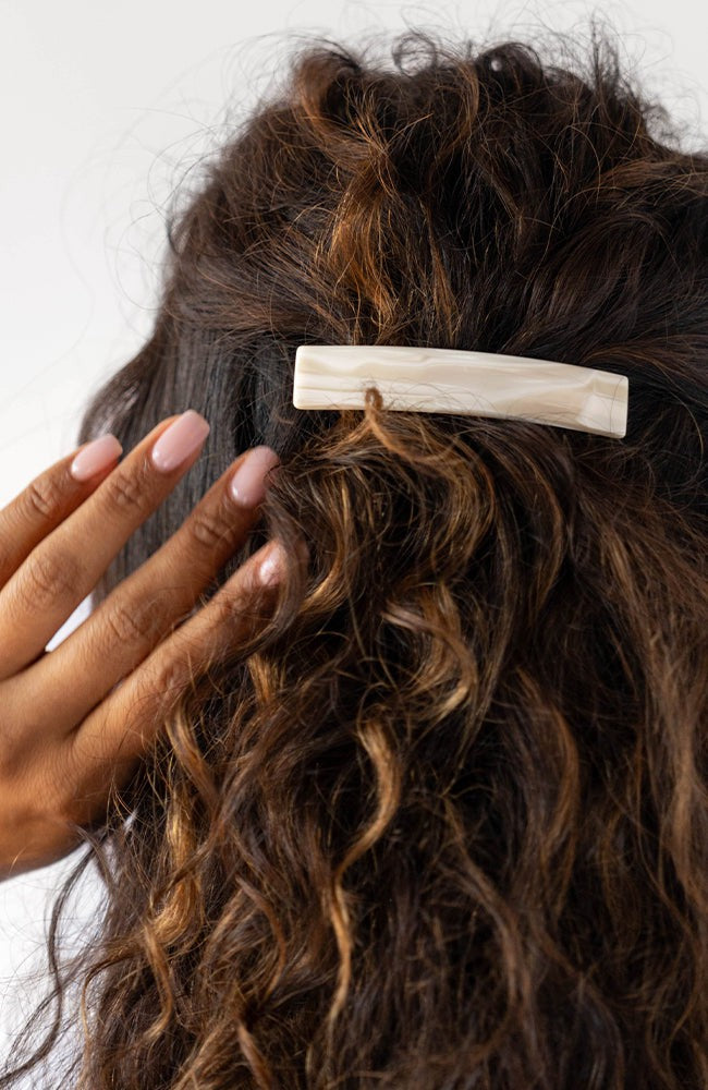 France Luxe medium French barrette for women pictured holding curly, brown hair in a half up hairstyle.