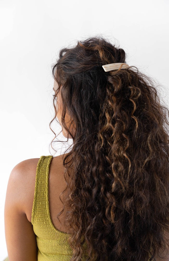 France Luxe medium, white barrette for women pictured holding curly, brown hair in a half up hairstyle.