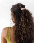 France Luxe medium, white barrette for women pictured holding curly, brown hair in a half up hairstyle.