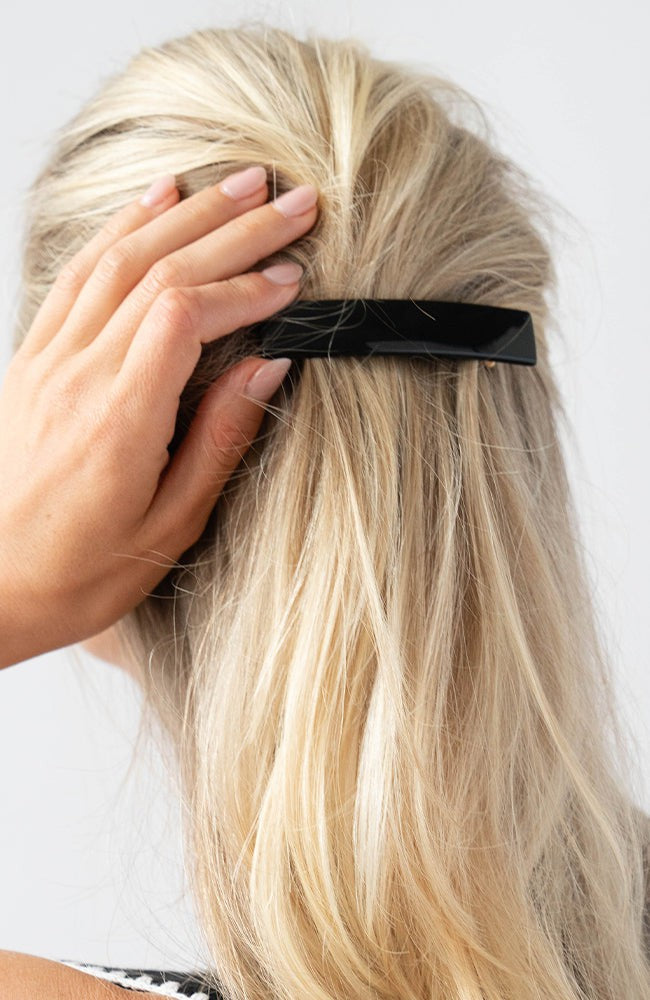 France Luxe medium, black barrette for women pictured holding straight, blonde hair in a half up hairstyle.