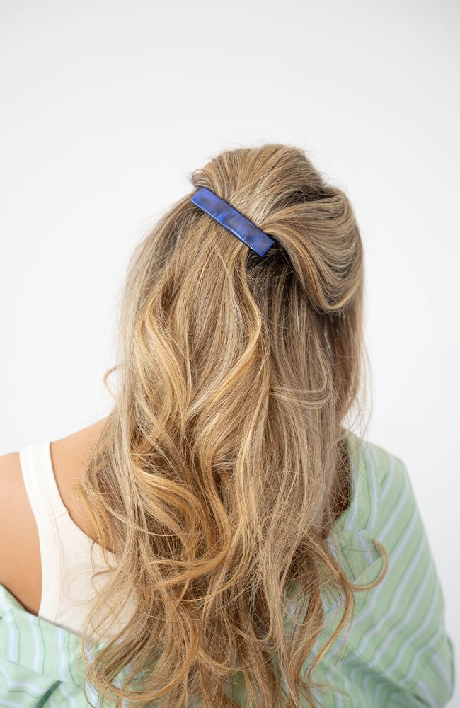 France Luxe medium, navy blue barrette for women pictured holding wavy, blonde hair in a casual half up hairstyle.
