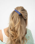 France Luxe medium, navy blue barrette for women pictured holding wavy, blonde hair in a casual half up hairstyle.