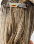 France Luxe medium French barrette for women pictured holding straight, blonde hair in a half up hairstyle.