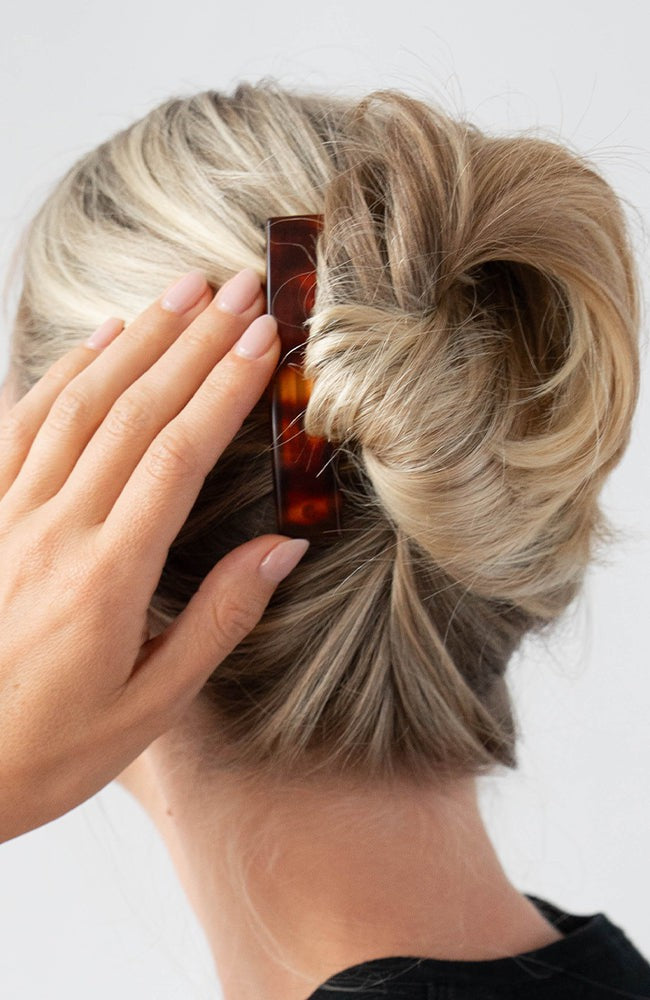 Woman with straight, blonde hair styled in an updo with a France Luxe medium barrette, rich amber and mahogany brown.