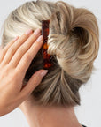 Woman with straight, blonde hair styled in an updo with a France Luxe medium barrette, rich amber and mahogany brown.