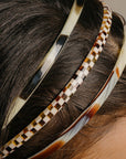 France Luxe thin headband in a Natural Horn, Black Horn, and Damier color, pictured holding straight, black hair in a loose hairstyle.