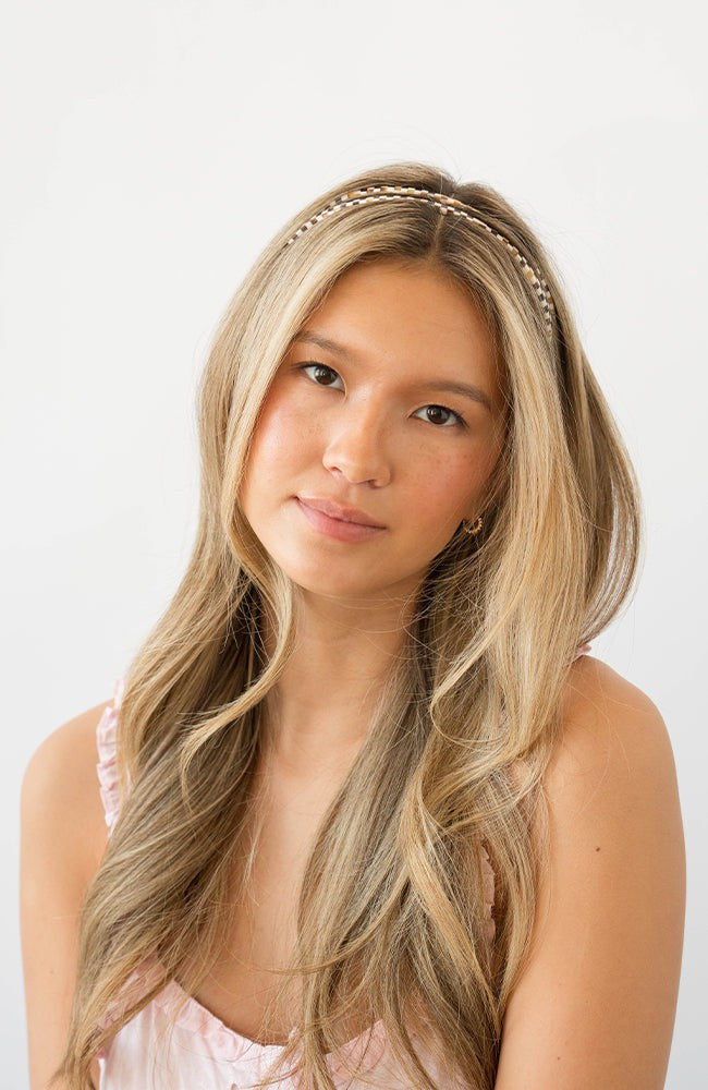 France Luxe thin headband in a checkered tortoise and ivory color, pictured holding straight, blonde hair in a loose hairstyle.