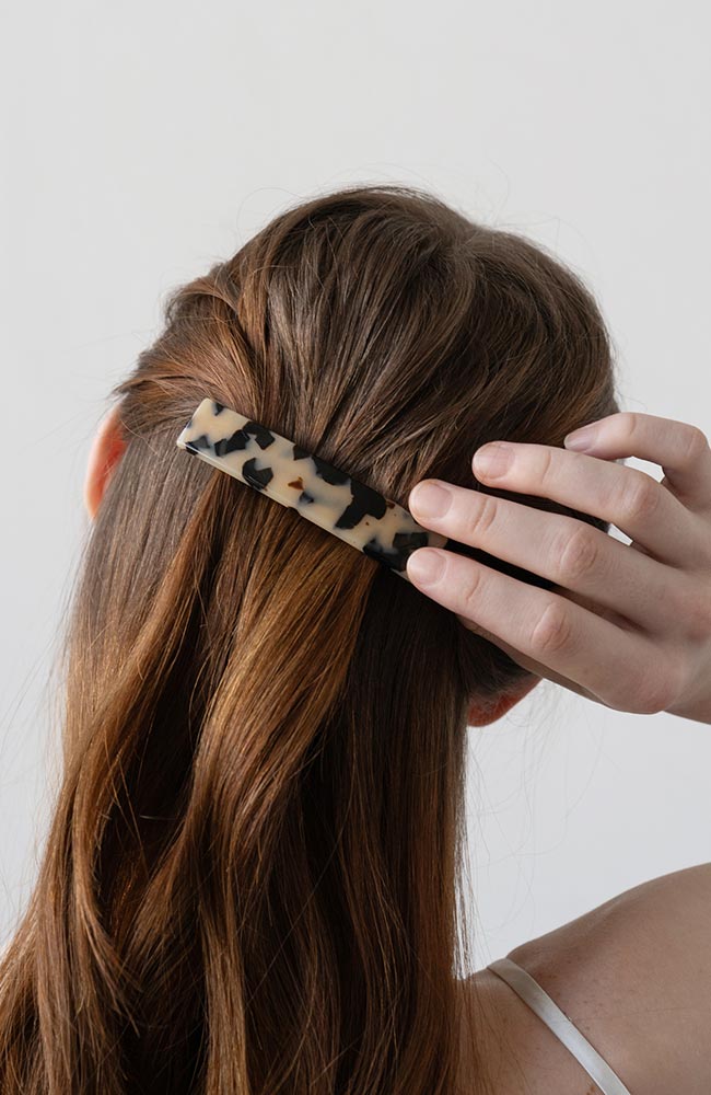 France Luxe medium French barrette for women pictured holding straight, brown hair in a half up hairstyle.