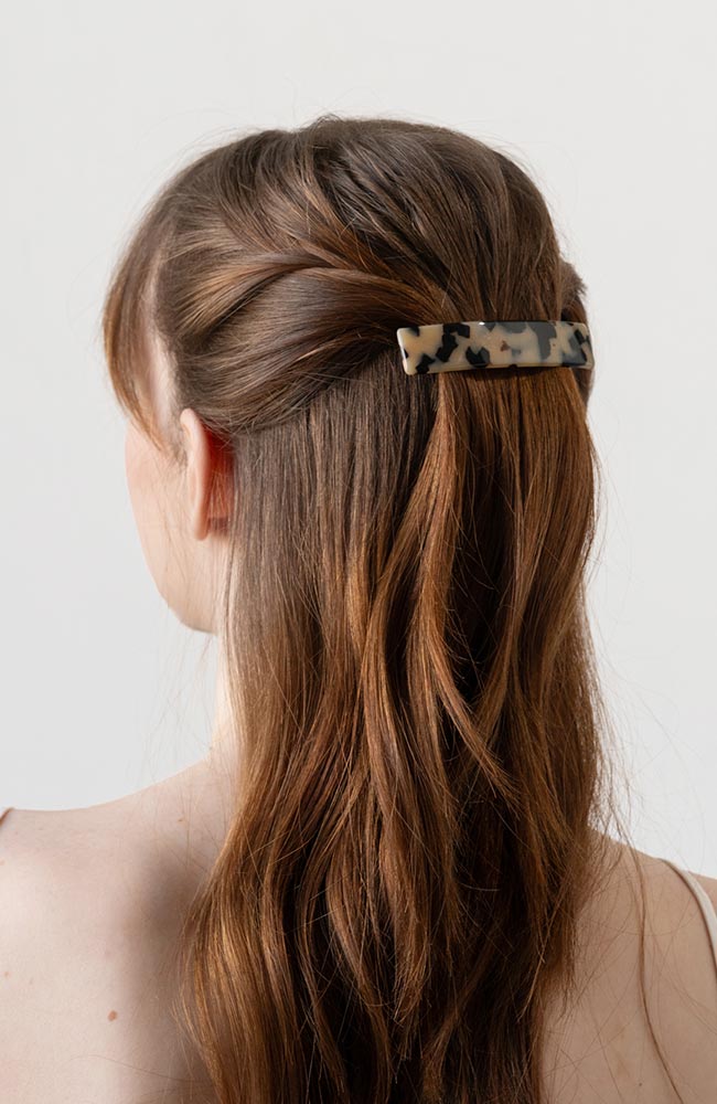 France Luxe medium French barrette for women pictured holding straight, brown hair in a half up hairstyle.