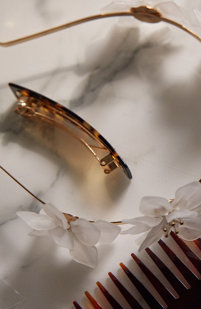Classic Tortoise French Barrette, with a white flower headband and wide tooth comb on a counter.