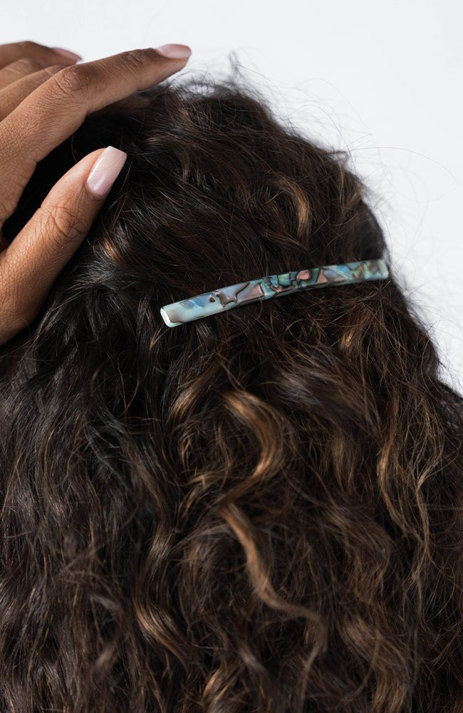 France Luxe long French barrette for women pictured holding curly, brown hair in a half up hairstyle.