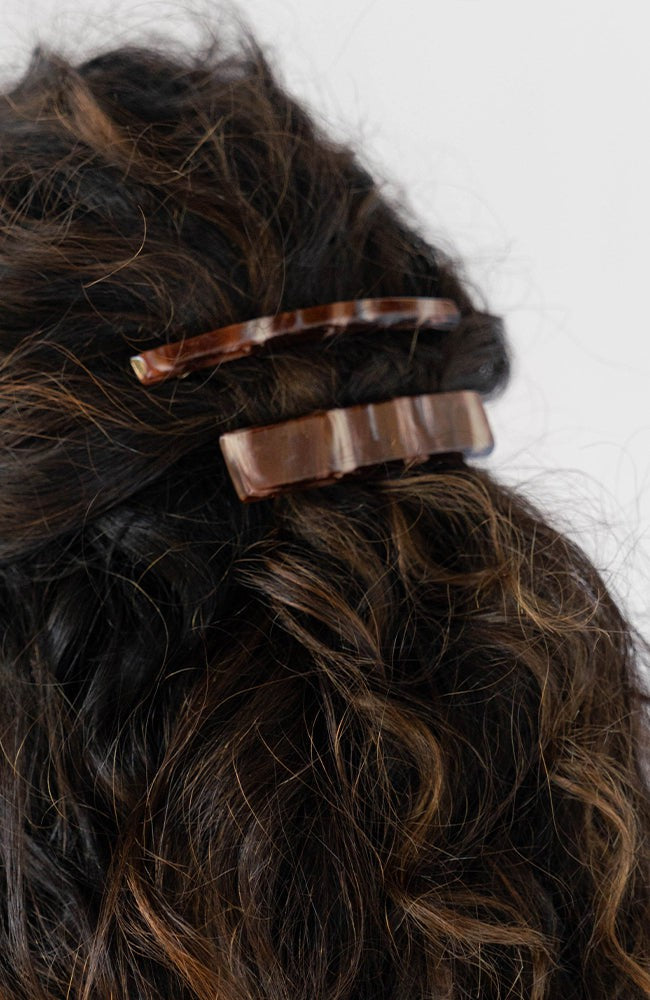 France Luxe long French barrette for women pictured holding curly, brown hair in a half up hairstyle.