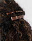 France Luxe long French barrette for women pictured holding curly, brown hair in a half up hairstyle.
