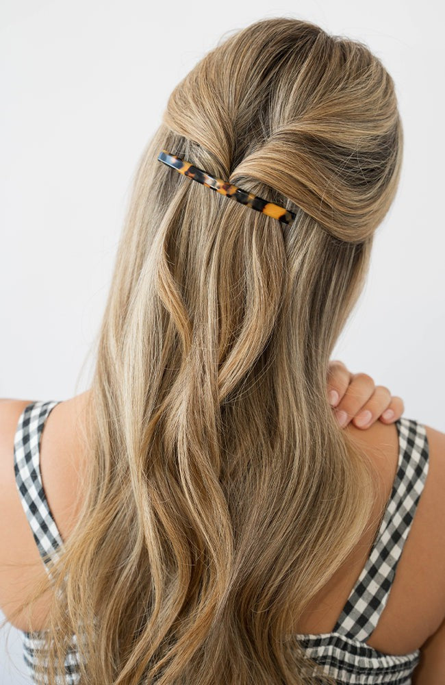 France Luxe long, classic tortoiseshell barrette for women pictured holding wavy, blonde hair in a half up hairstyle.