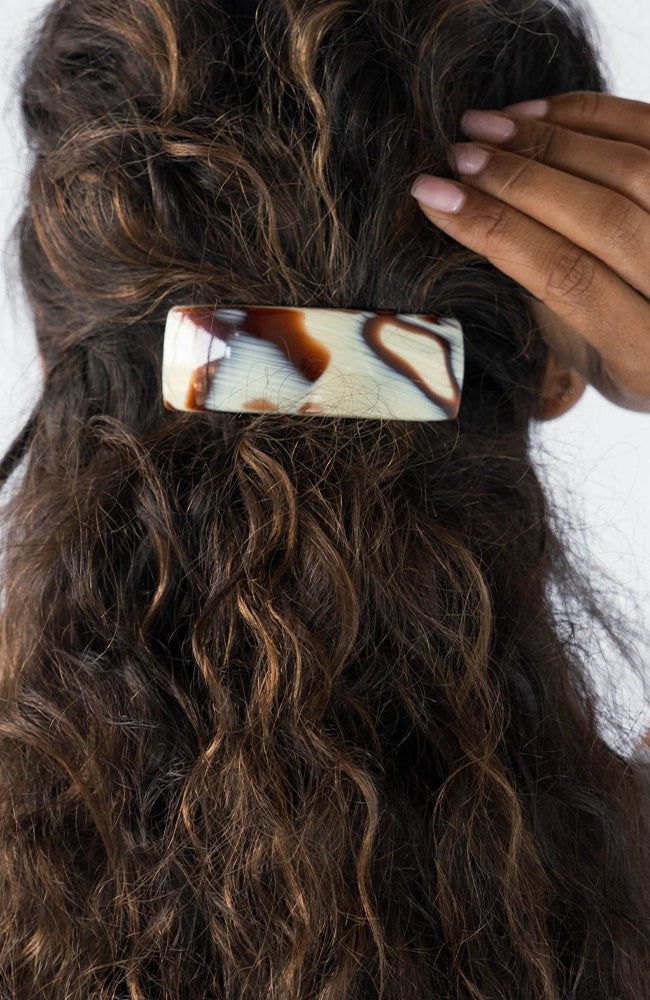 France Luxe large French barrette for women pictured holding curly, brown hair in a half up hairstyle.
