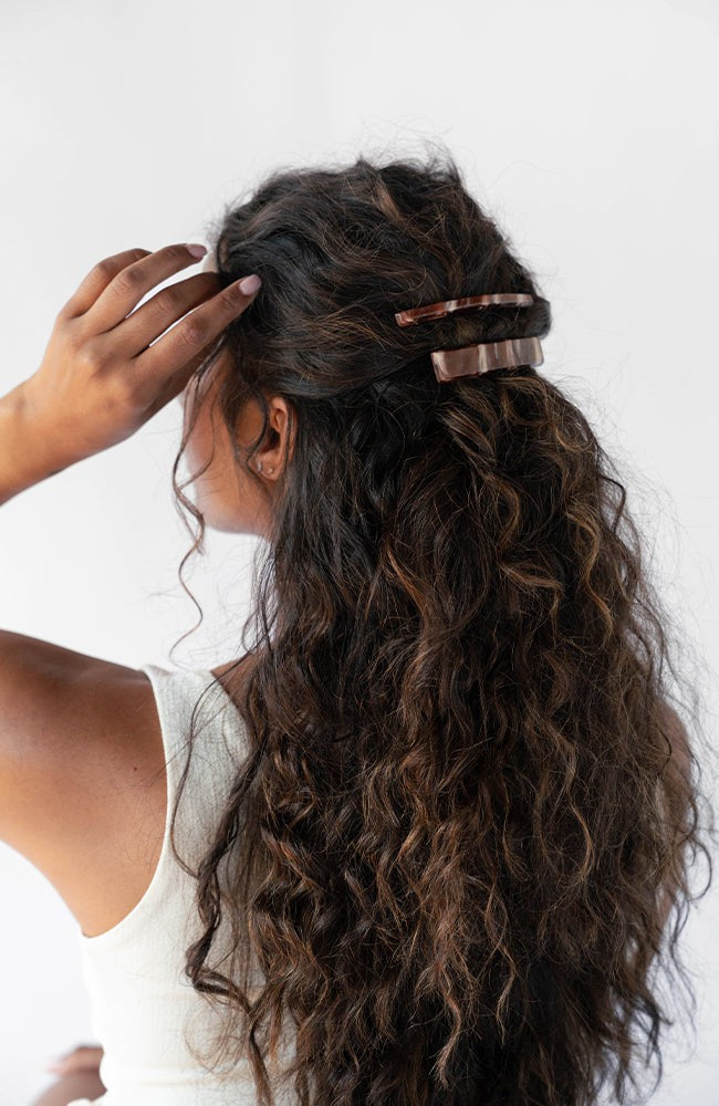 France Luxe medium French barrette for women pictured holding curly, brown hair in a half up hairstyle.