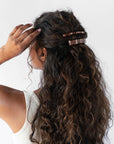 France Luxe medium French barrette for women pictured holding curly, brown hair in a half up hairstyle.