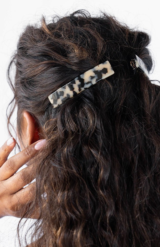 France Luxe medium French barrette for women pictured holding curly, brown hair in a half up hairstyle.