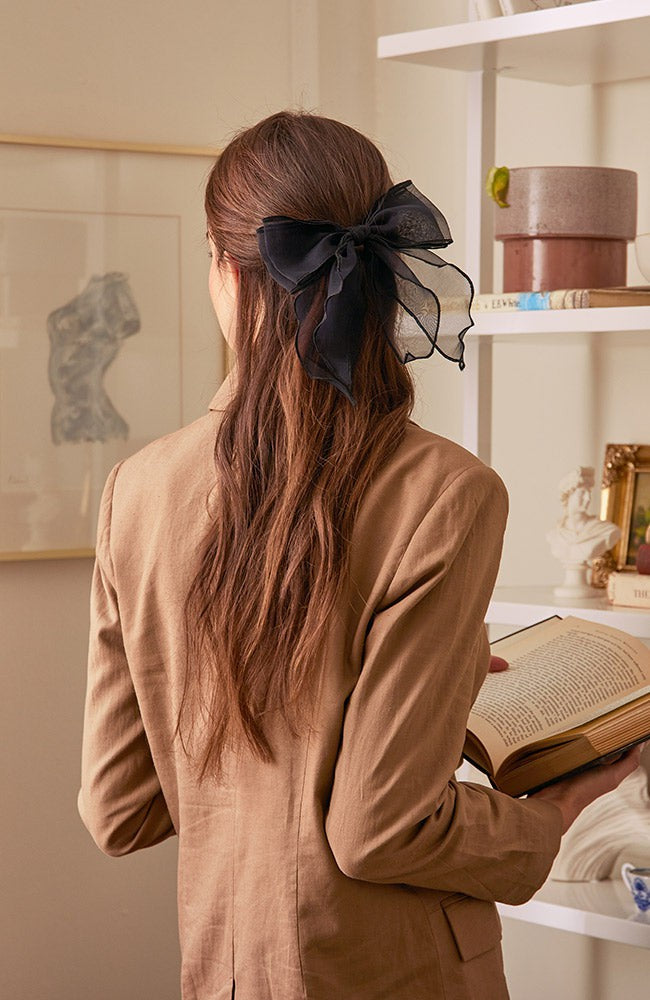 Black chiffon bow hair accessory in brown hair. Young woman is reading, wearing a brown linen blazer.