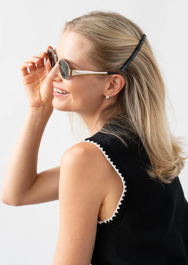 Woman wearing a black French barrette hair clip, sunglasses, and a black and white top, with a plain background.
