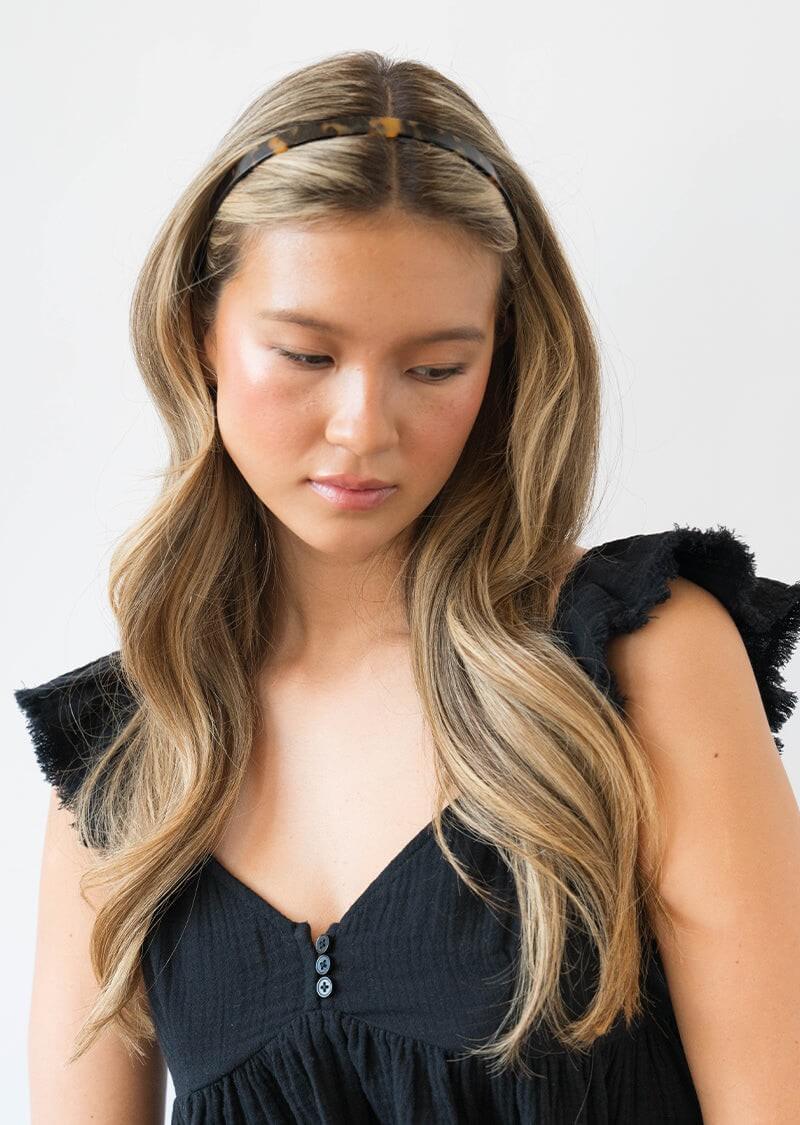 Woman with long, wavy hair wearing a tortoise headband for women and black dress
