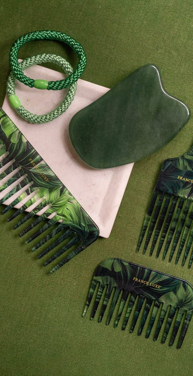 Green hair pick, green wide tooth combs, green jade tool, and green hair tie bracelets on a green background