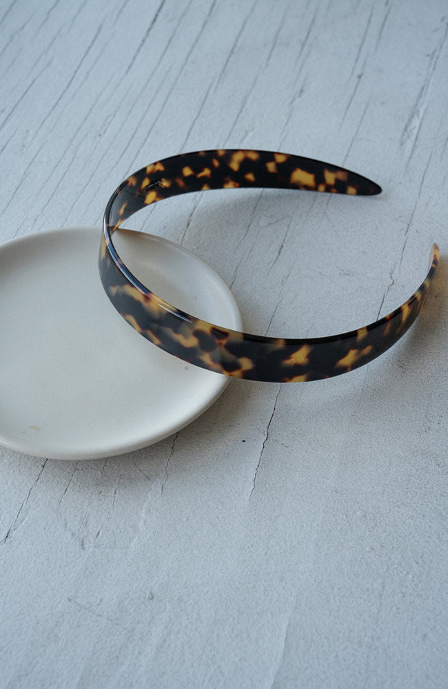 Elegant French Headband in a Classic Tortoiseshell pattern, pictured resting on a table.