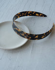 Elegant French Headband in a Classic Tortoiseshell pattern, pictured resting on a table.